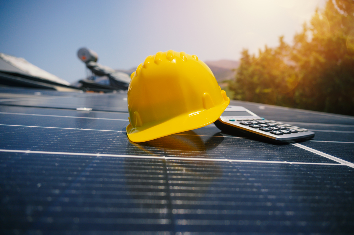 Yellow hard hat and calculator on rooftop solar panels representing a solar savings calculator for estimating energy bill reduction.